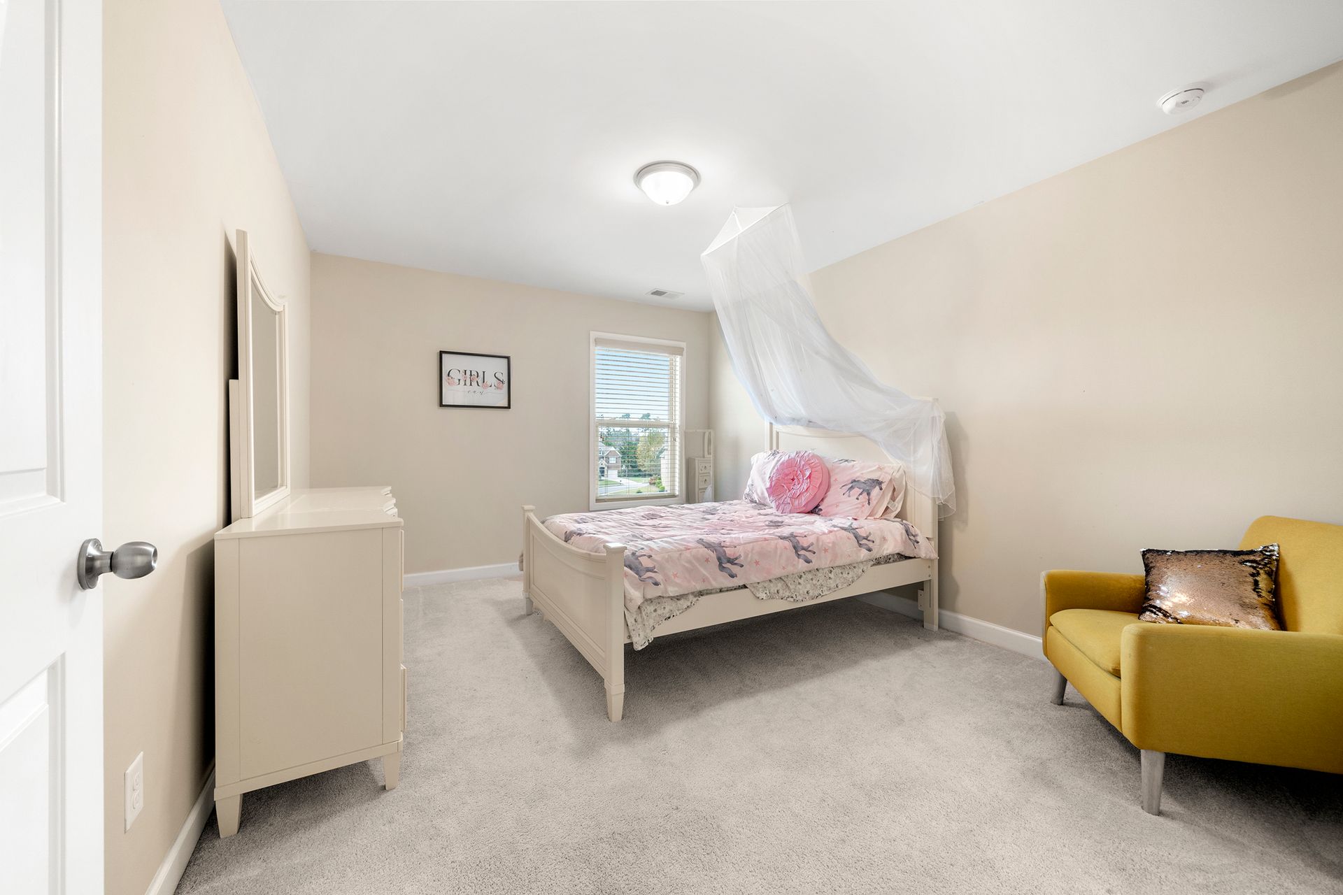 A bedroom with a bed , chair , dresser and mirror.