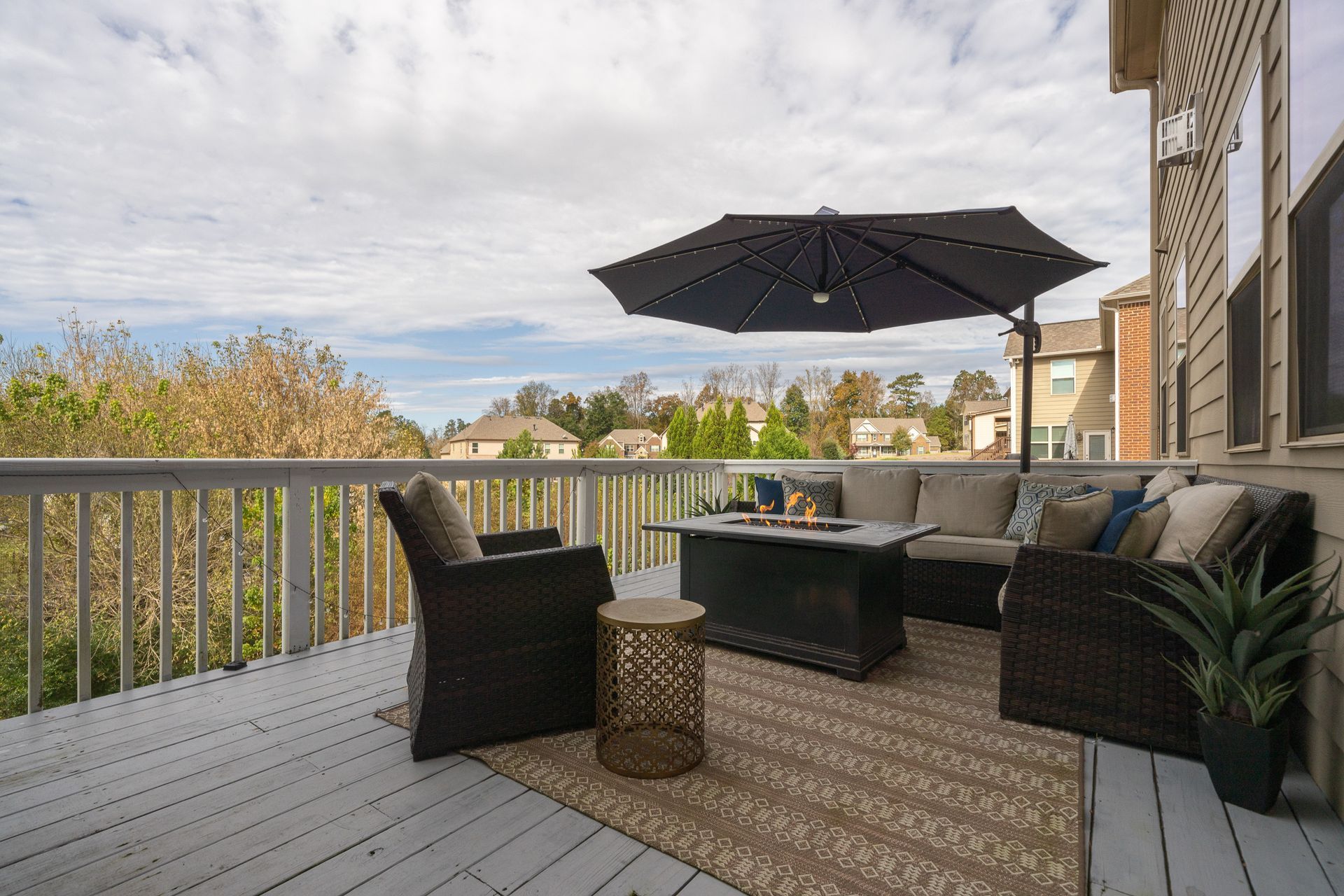A deck with a couch , chairs , umbrella and fire pit.