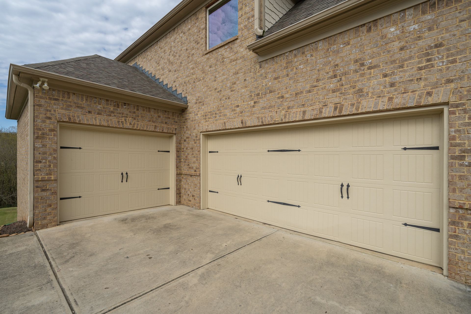 There are two garage doors on the side of a brick house.