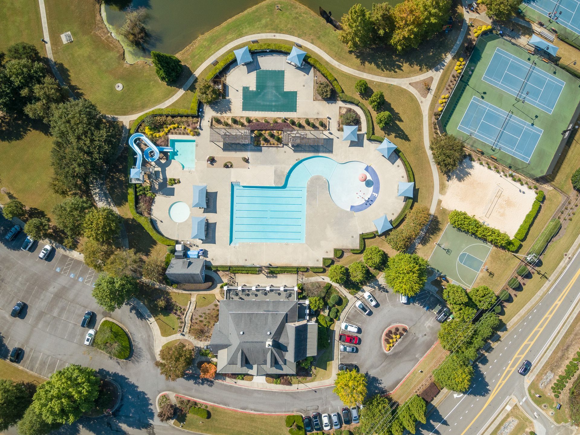 An aerial view of a swimming pool and tennis courts in a park.