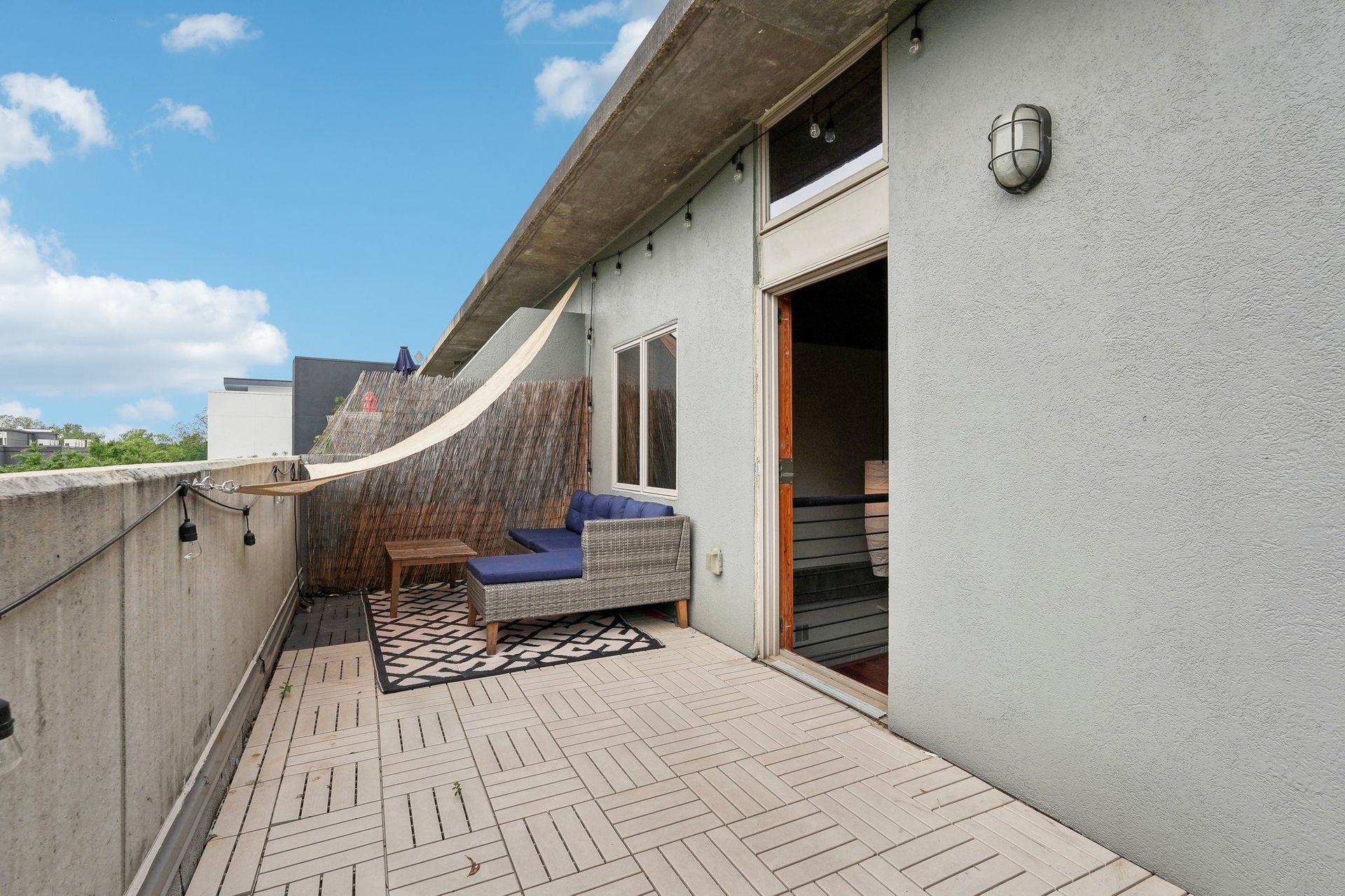 Balcony with wooden flooring, seating, and open doorway, blue sky background.