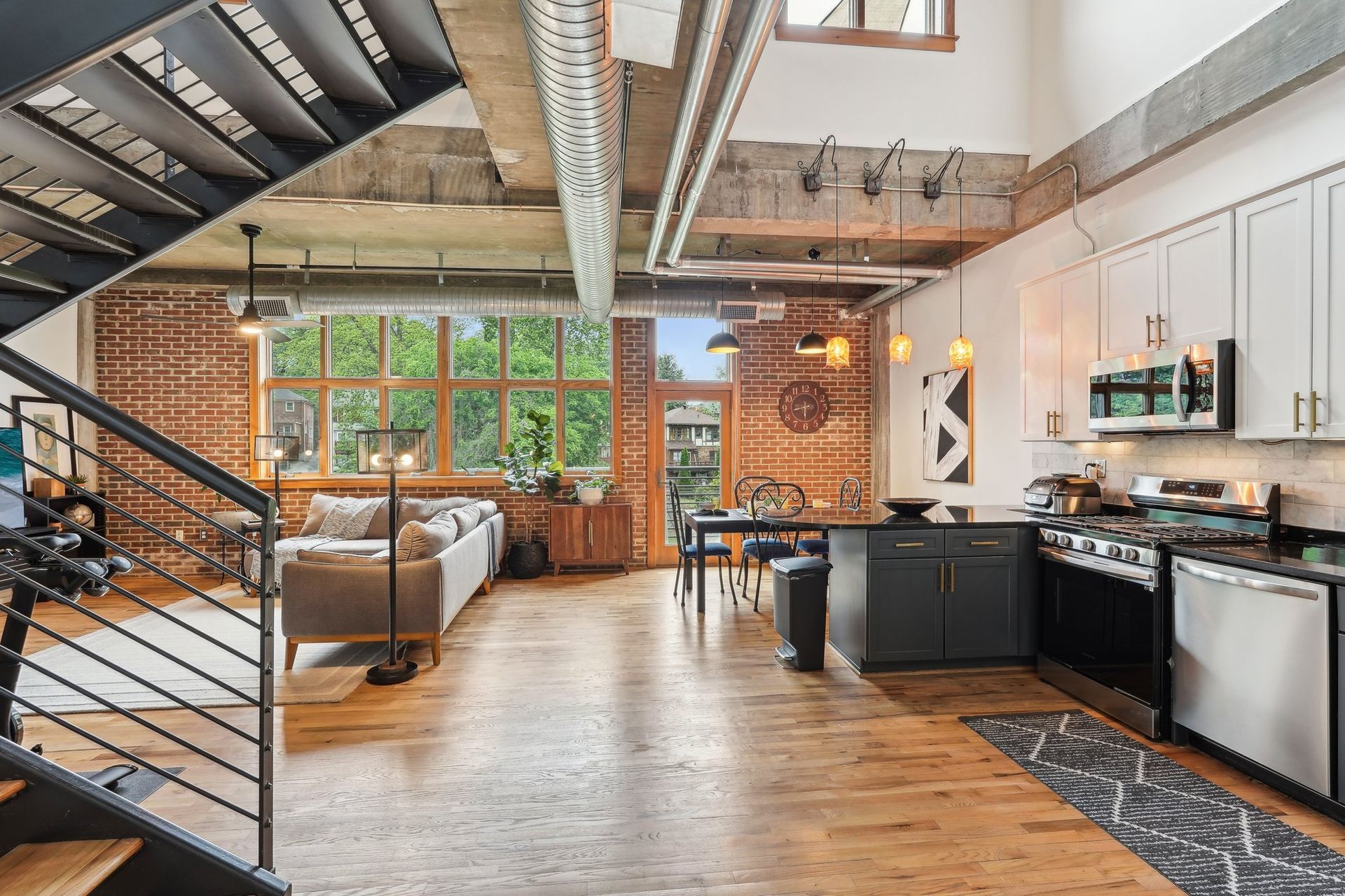 Loft apartment interior with exposed brick, metal staircase, kitchen, and living area.