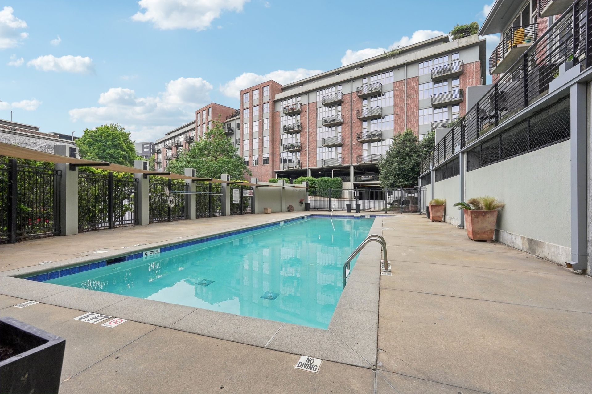Pool with clear water in front of a modern apartment building under a blue sky.