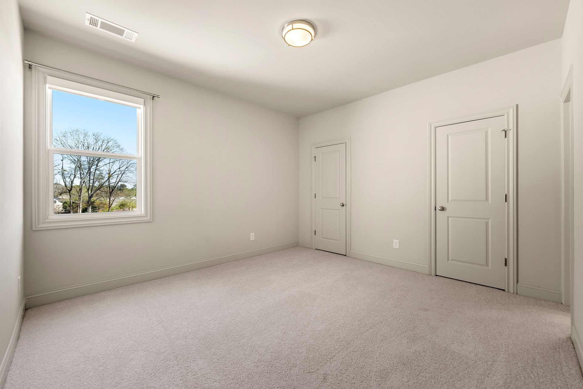 An empty bedroom with a window and a carpeted floor.