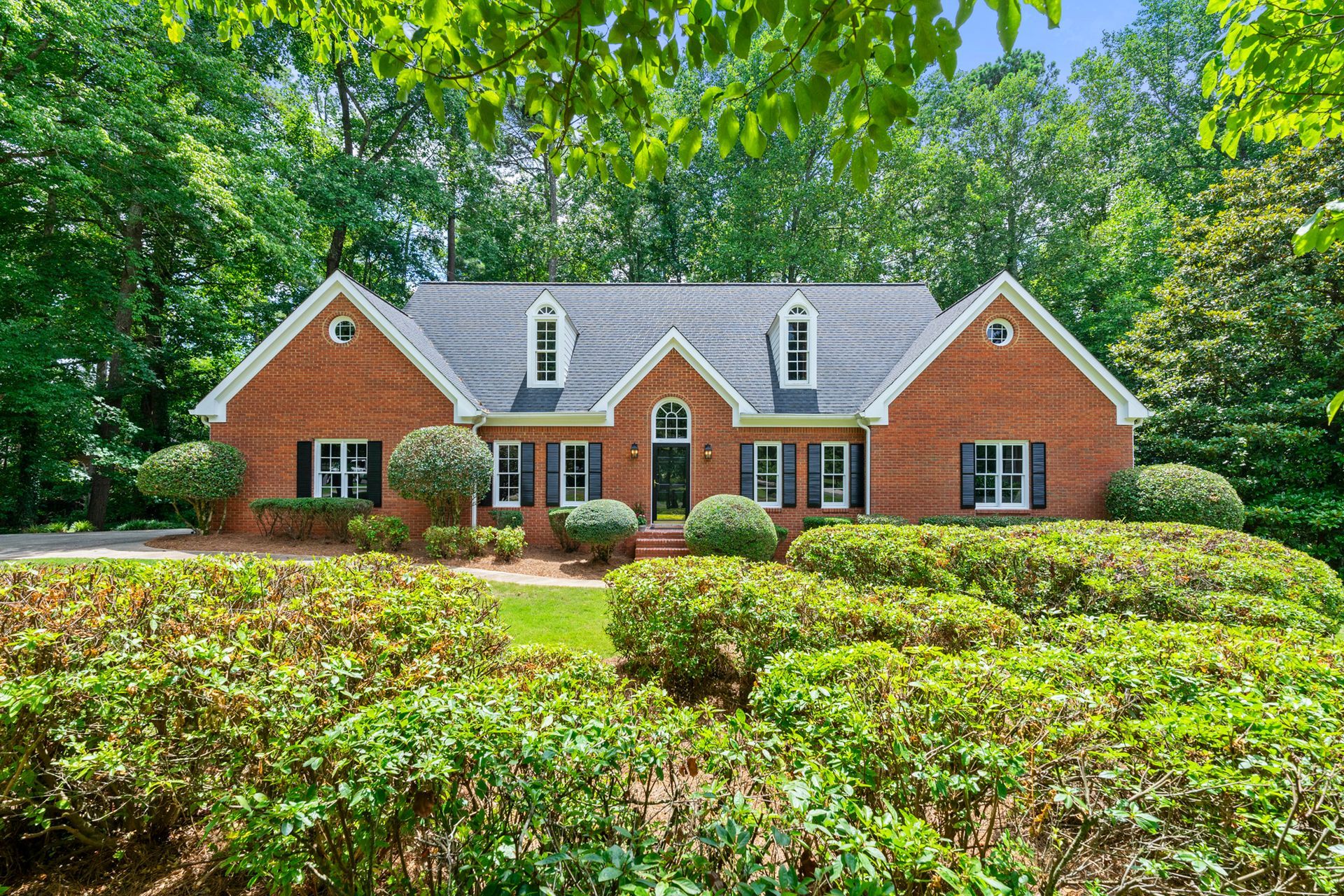 A large brick house with a blue roof is surrounded by trees and bushes.