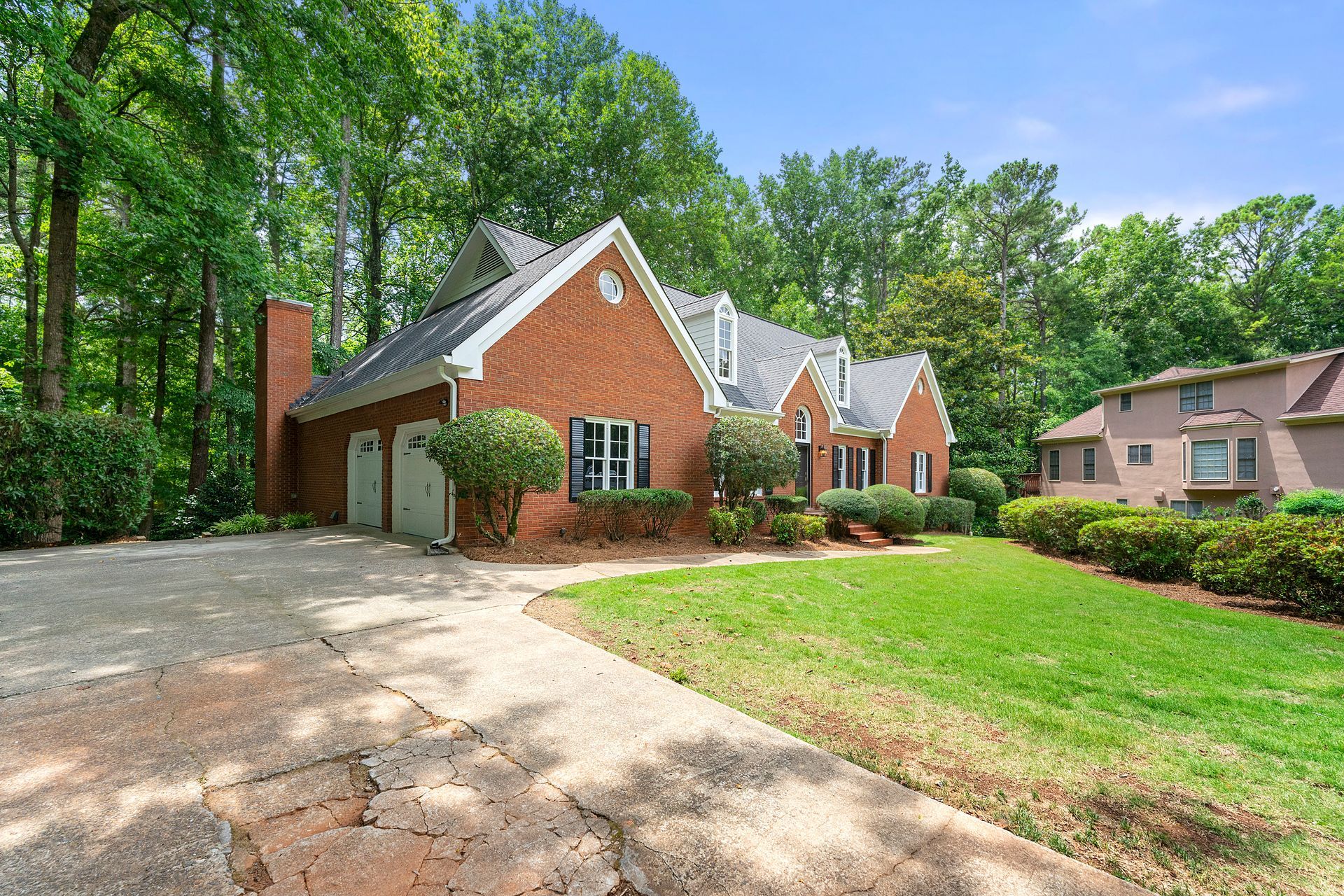 A large brick house with a large driveway in front of it surrounded by trees.