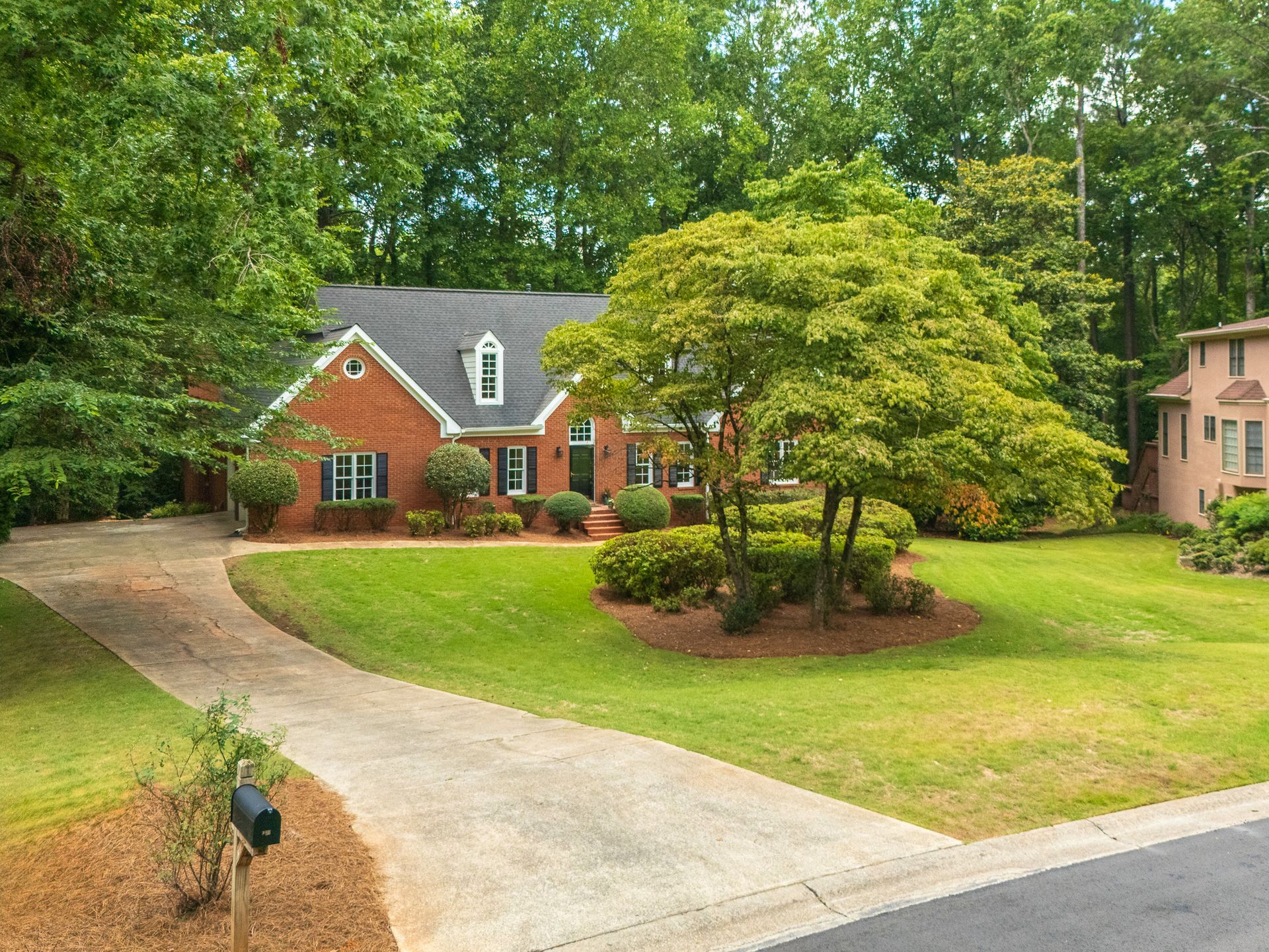 A brick house with a lush green lawn and a driveway leading to it.