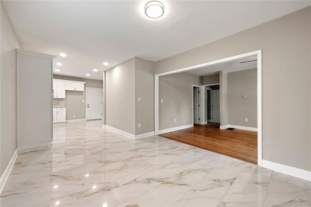 An empty living room with a marble floor and a kitchen in the background.
