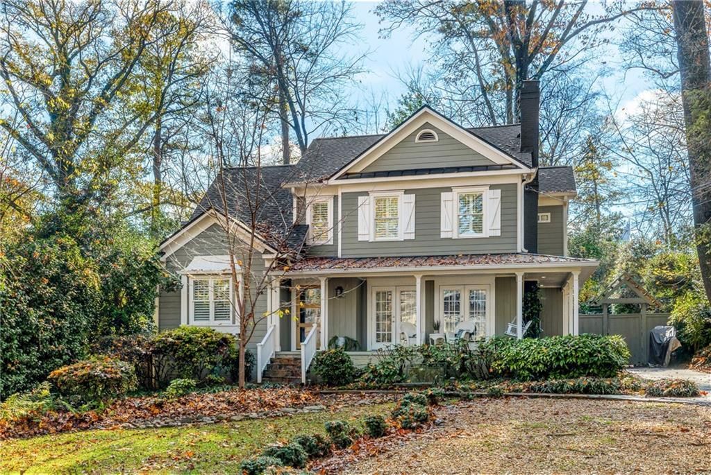 Two-story house with green siding, white trim, and a small porch, surrounded by trees and bushes.