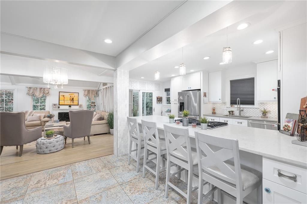 White cabinetry, island with bar stools, stainless steel appliances, and neutral furniture.