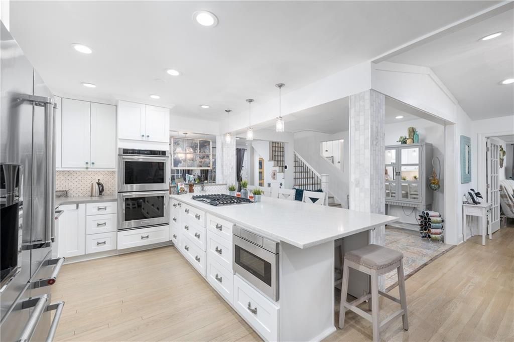 Bright white kitchen with island, stainless steel appliances, and adjacent open living space.