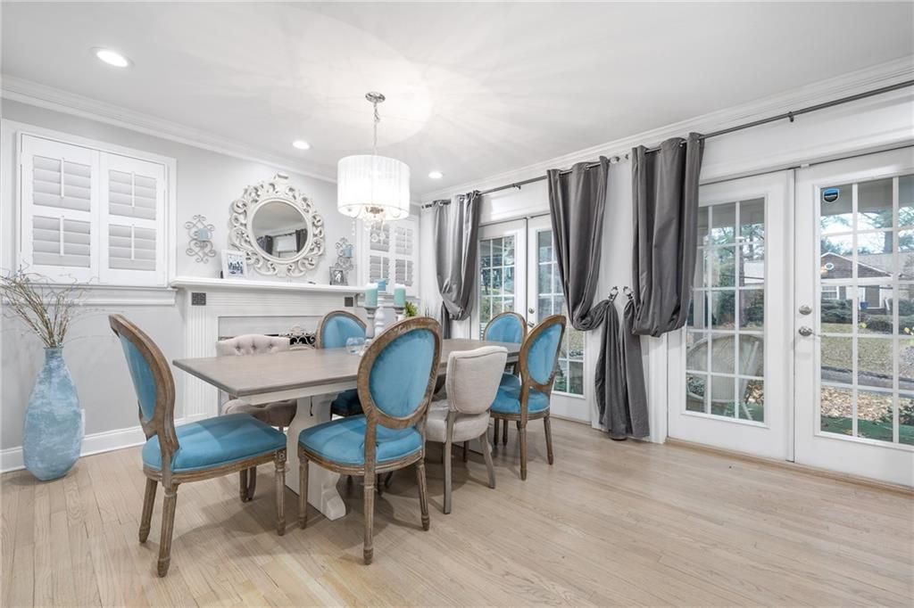 Dining room with light wood floors, blue chairs, white table, and large French doors with gray curtains.