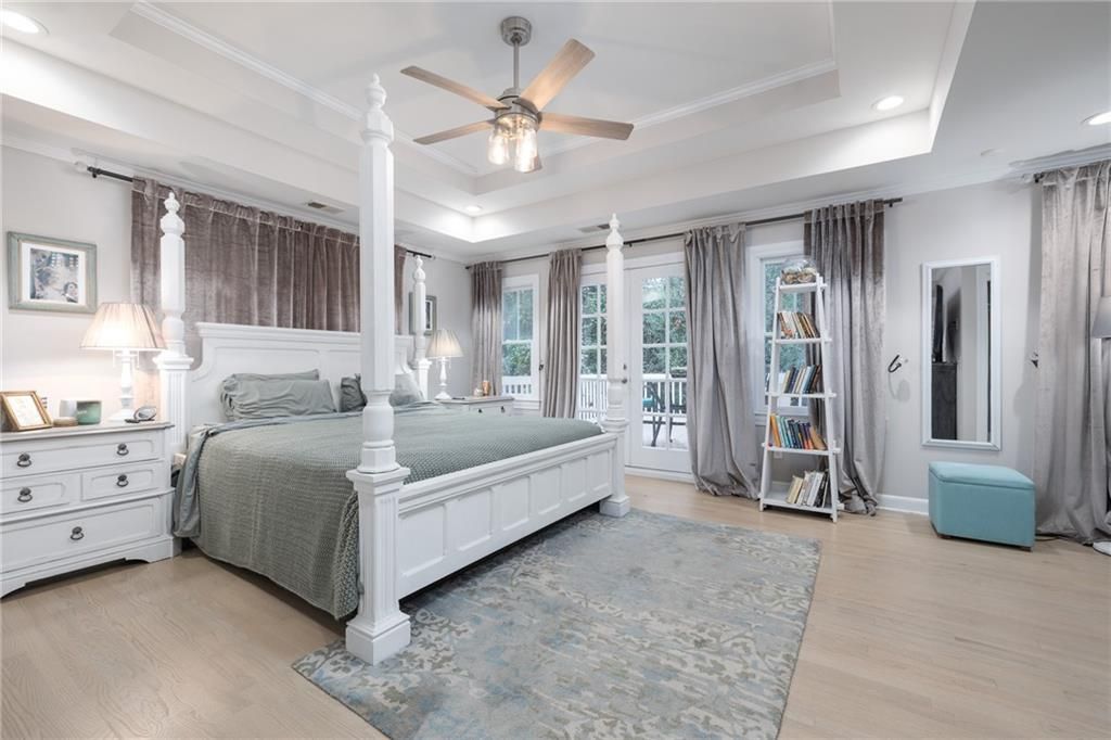 Spacious white bedroom with a four-poster bed, light blue rug, and gray curtains.