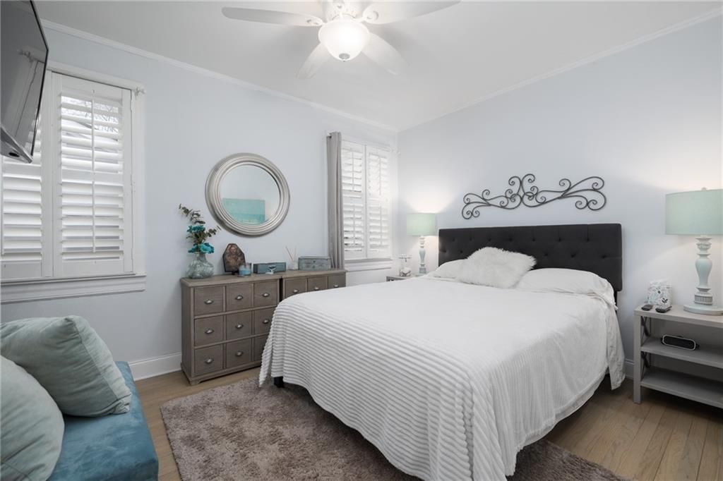 Bedroom with a bed, dresser, mirror, and shutters. Light blue walls and wood floors.