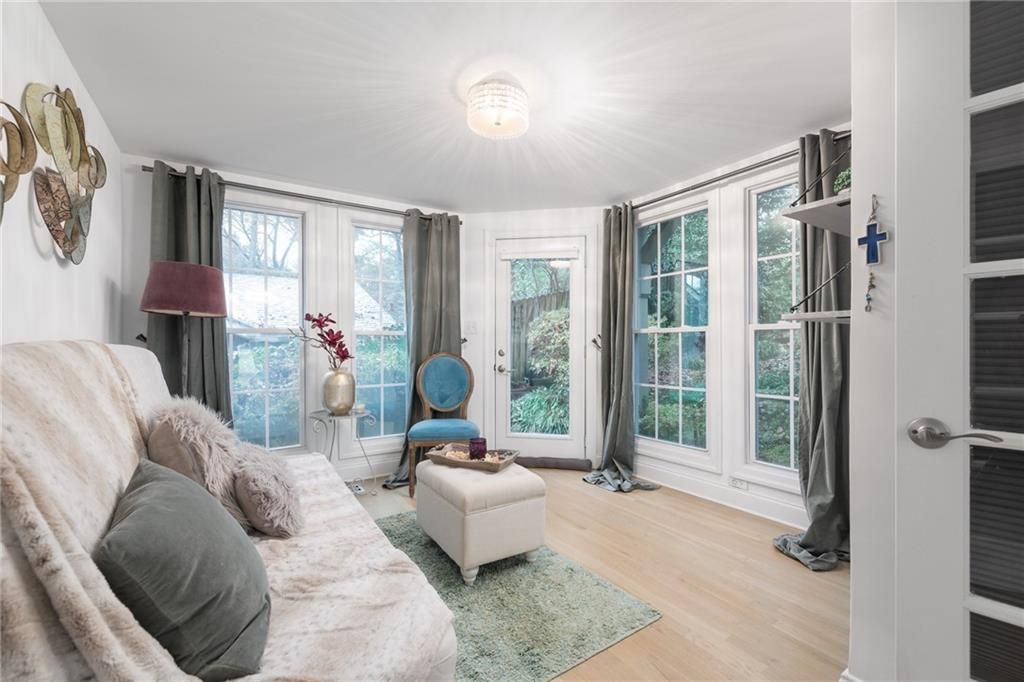 Bright living room with windows, light wood floor, neutral couch, and blue chair.