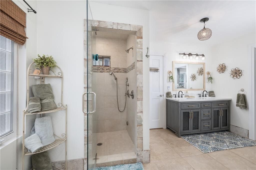 Bathroom with shower, vanity, and shelving; light colors with stone accents.