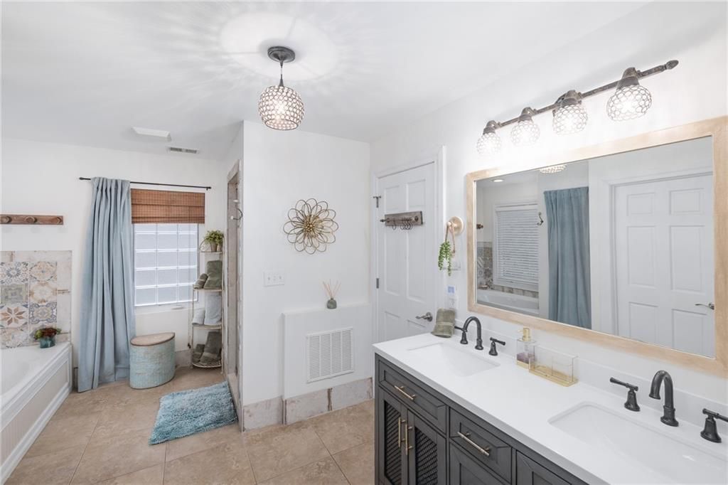 Bathroom with double vanity, mirror, tub, and shower, in a neutral palette with blue accents.