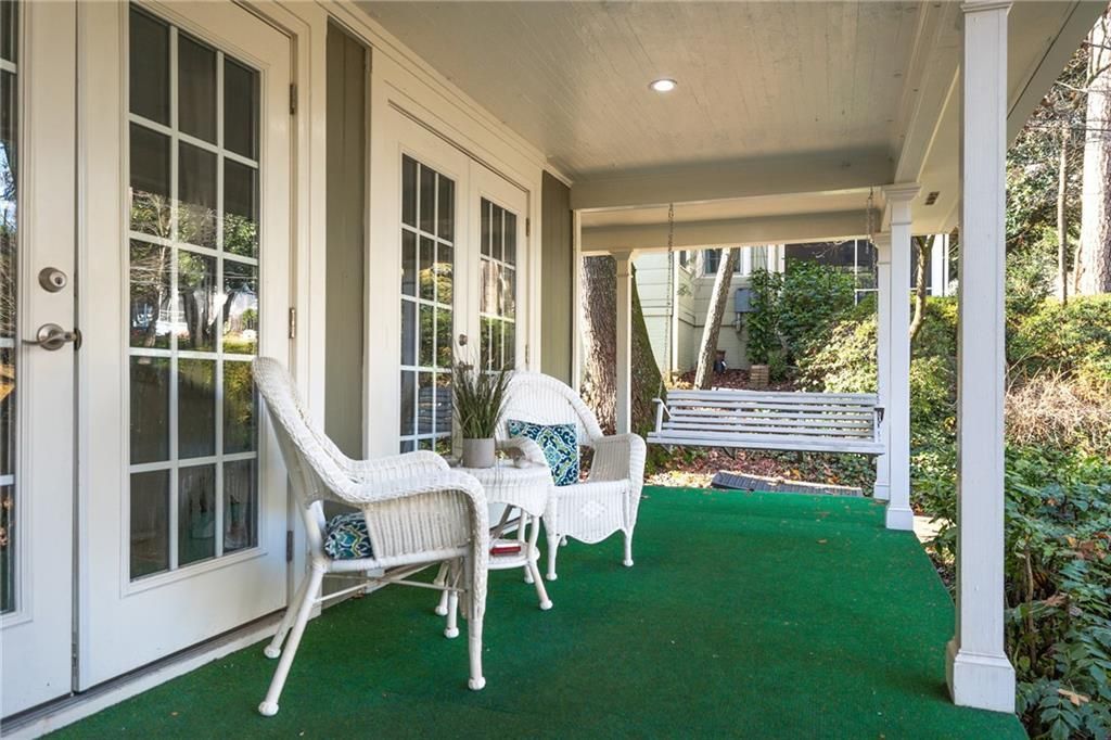 Covered porch with white wicker furniture, a swing, and green turf flooring.