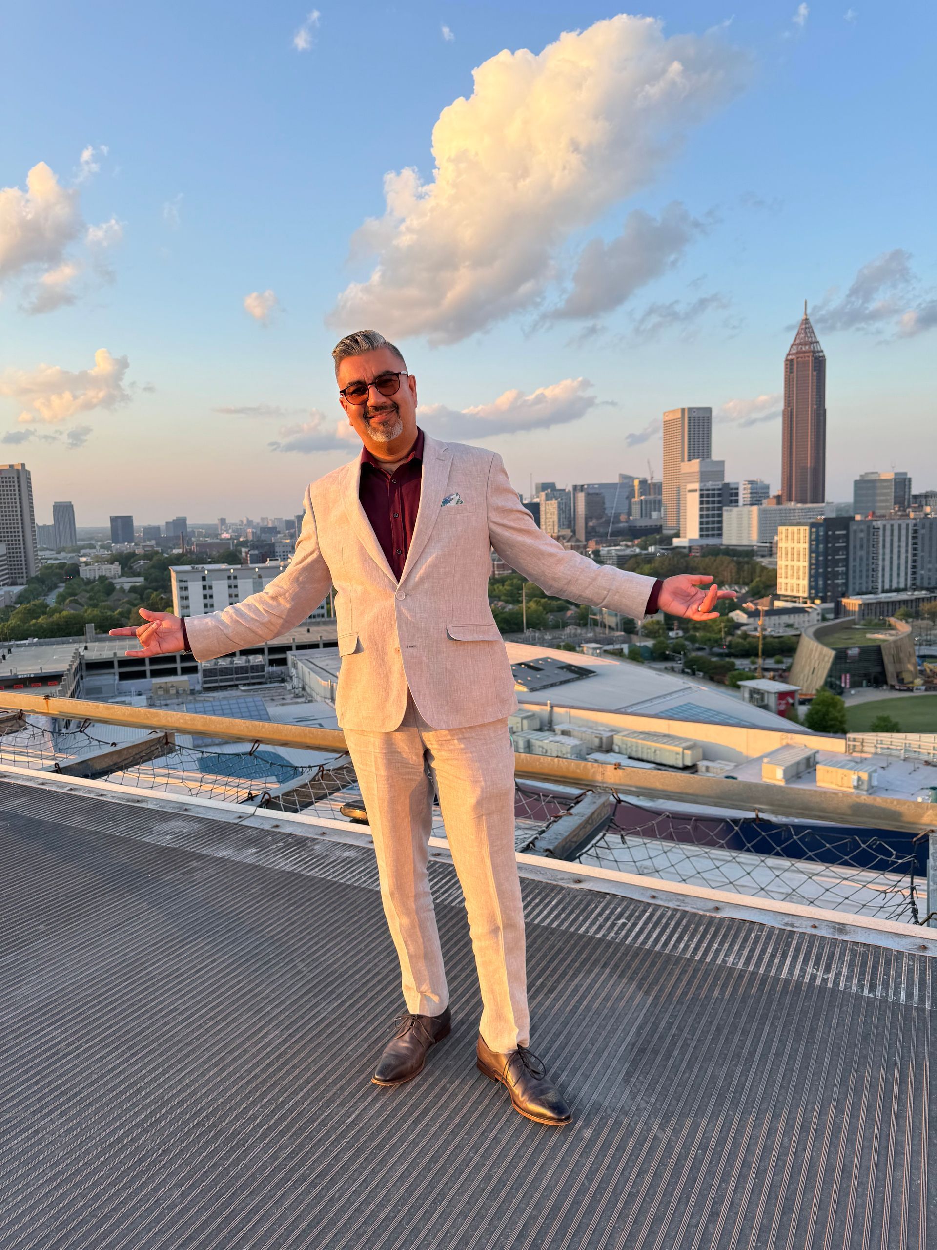A man in a suit is standing on top of a building with his arms outstretched.
