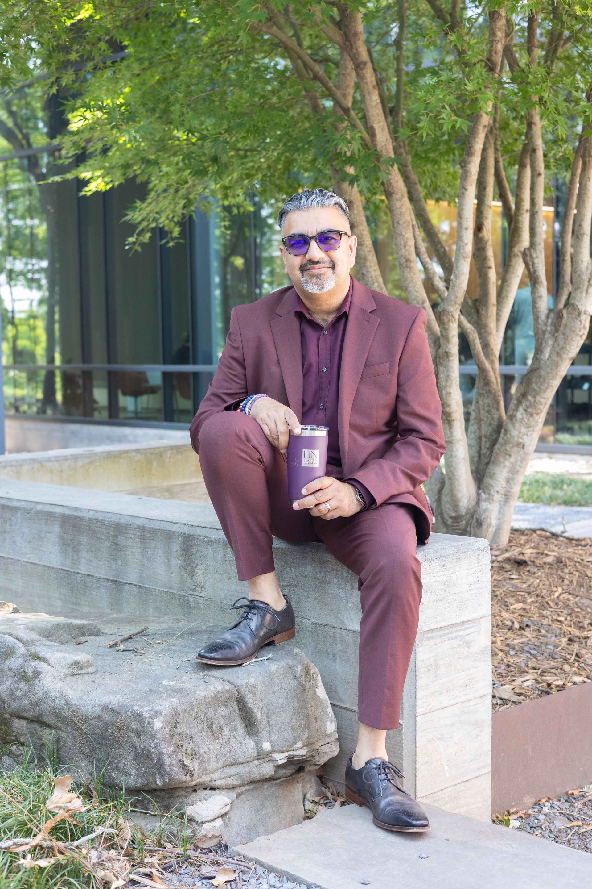 A man in a suit is sitting on a rock holding a cup of coffee.