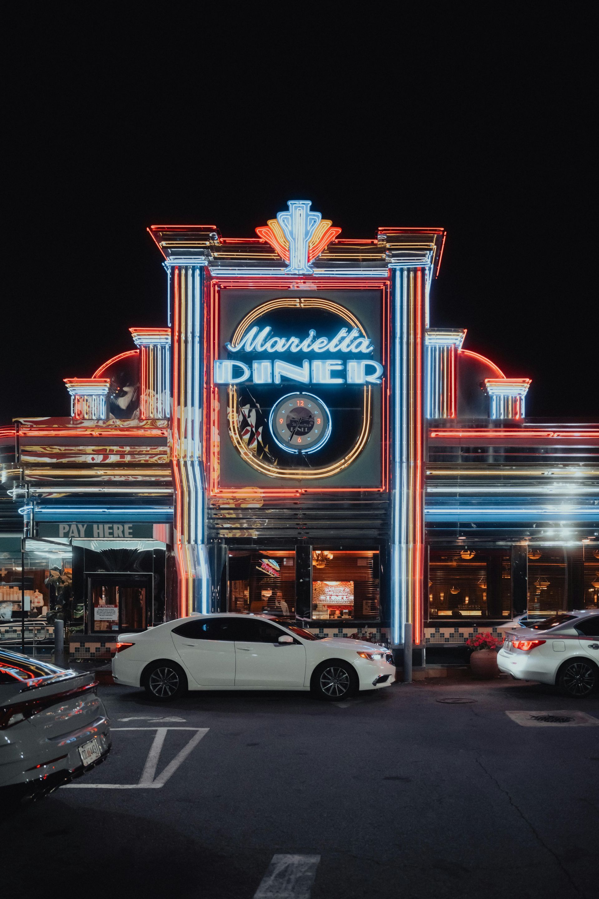 A diner is lit up at night with cars parked in front of it.