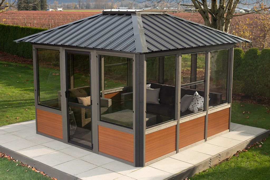 Gazebo with glass windows and a metal roof on a patio, with outdoor seating inside.
