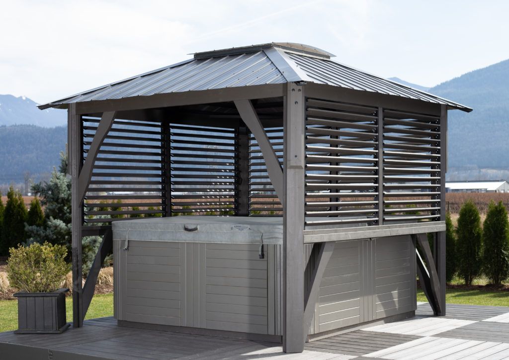 Gazebo with slatted walls and a metal roof over a hot tub on a patio.
