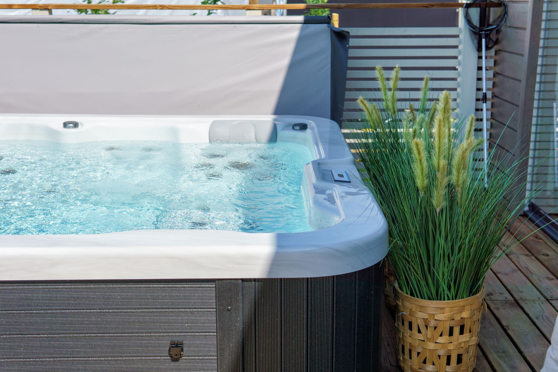 Modern backyard hot tubs with bubbling water on deck beside tall green plants and privacy screen