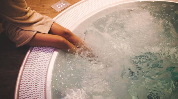 Person dipping legs in hot tub with bubbling water, wearing a bathrobe, relaxing at spa.