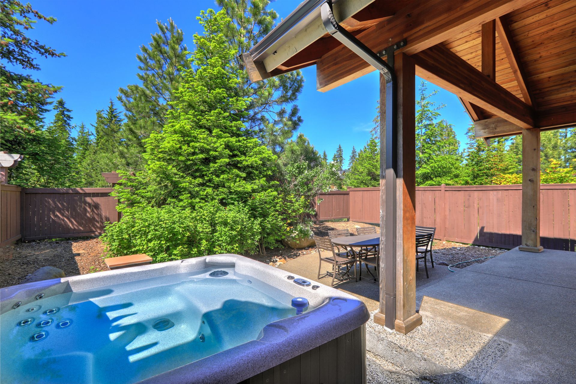 Small fenced back yard space with dining room table and hot tub.