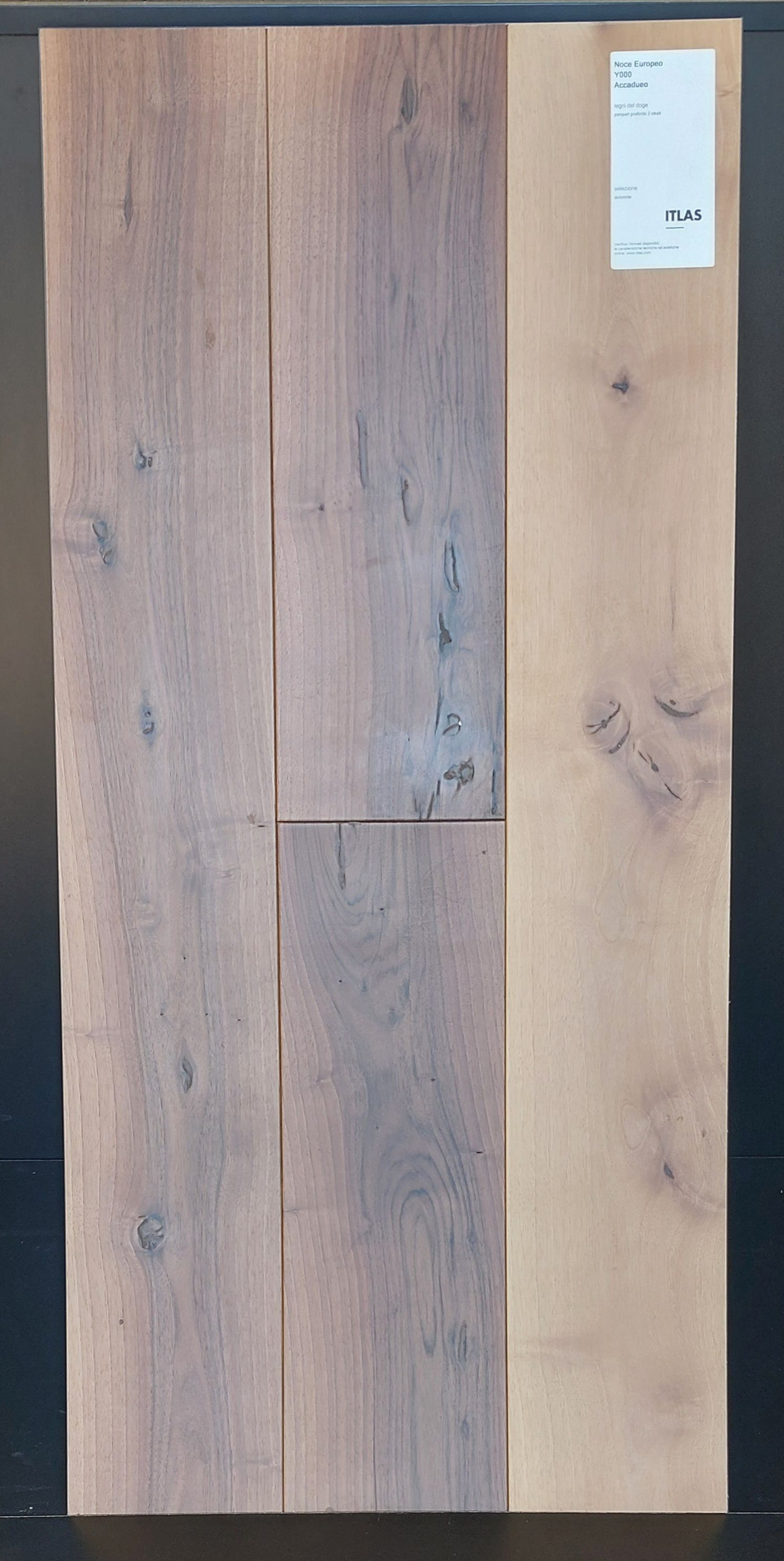 Tre assi di legno, due di tonalità più scura e una più chiara, con etichetta. Le assi sono strutturate e mostrano le venature del legno.