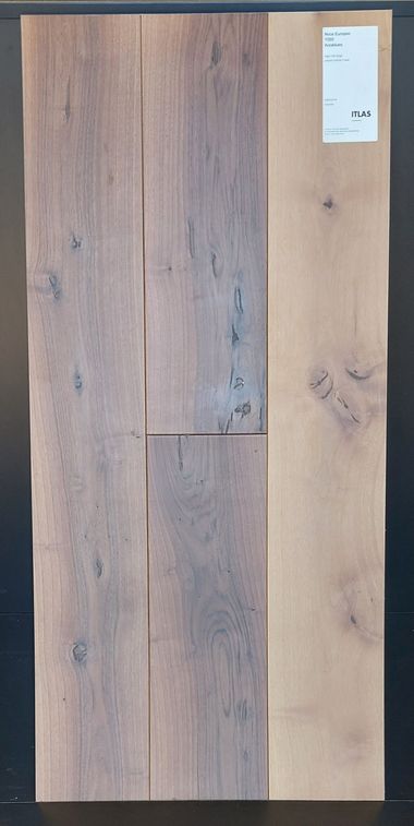 Tre assi di legno, due di tonalità più scura e una più chiara, con etichetta. Le assi sono strutturate e mostrano le venature del legno.