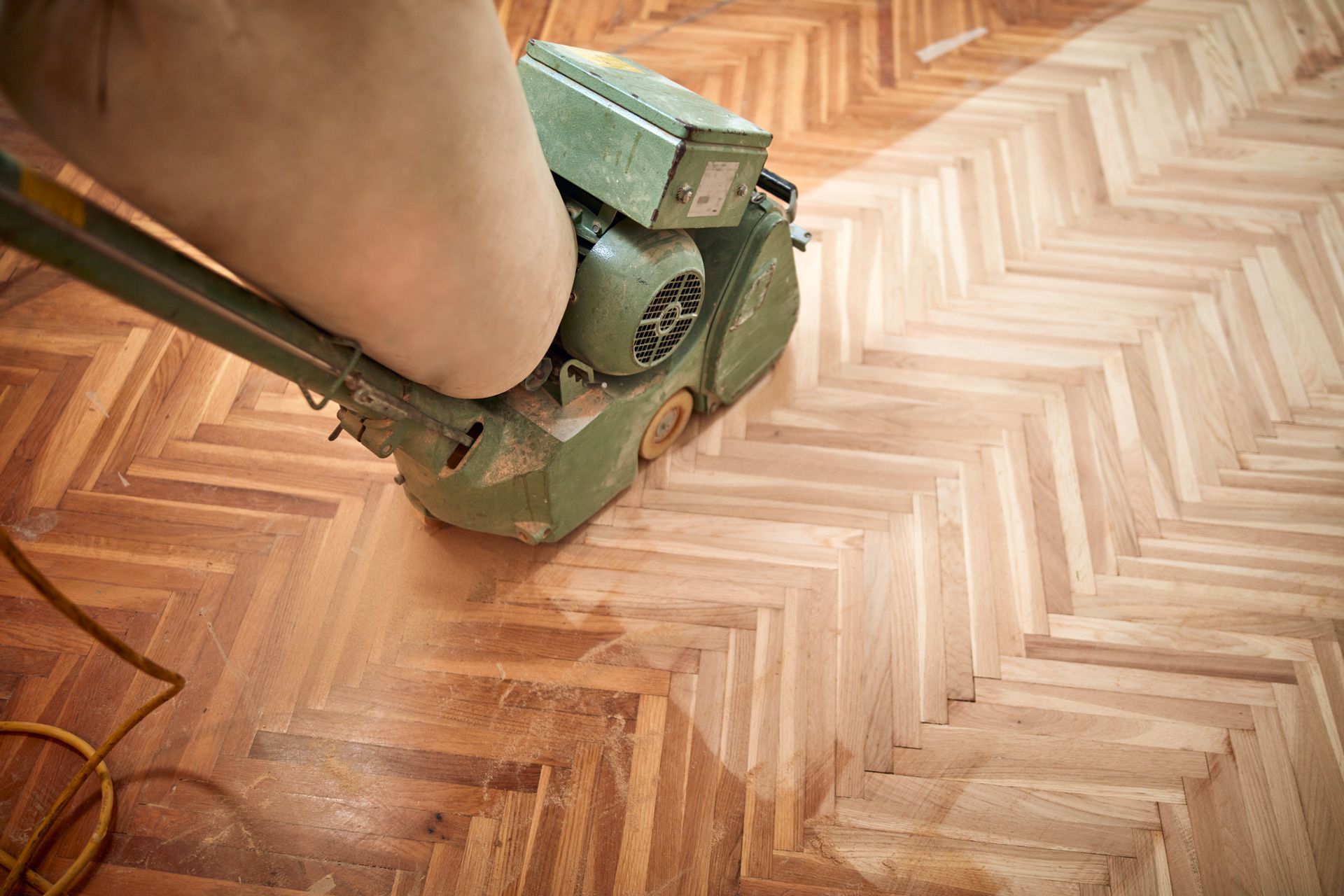 Persona che leviga un pavimento in parquet con una levigatrice per pavimenti verde, rivelando il legno più chiaro.