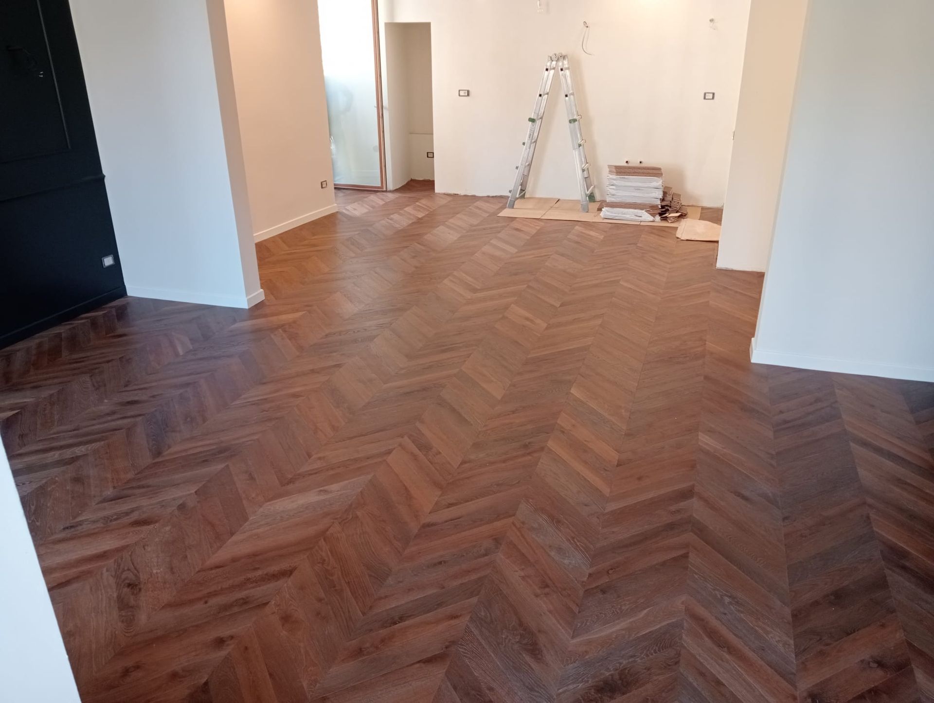 Pavimento in legno a spina di pesce in una stanza con pareti bianche che riflettono la luce.