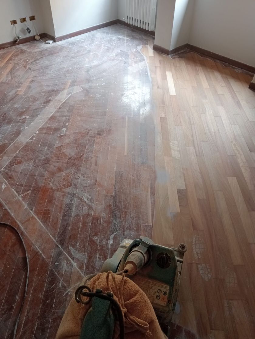 Pavimento in fase di levigatura in una stanza con luce naturale. L'area è stata parzialmente rifinita, rivelando un colore del legno più chiaro.