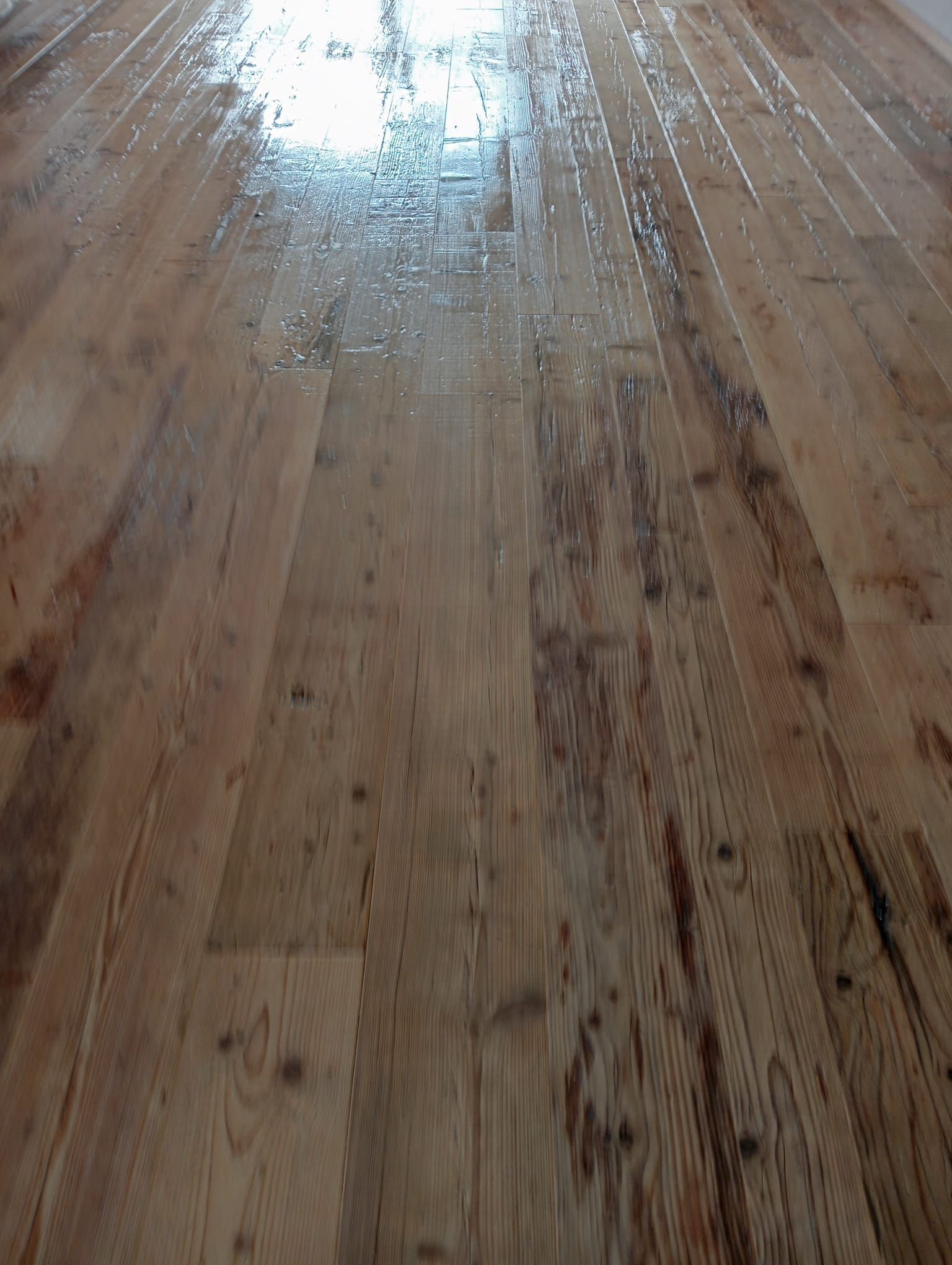 Pavimento in legno con finitura lucida, con venature e nodi evidenti nelle assi del legno.