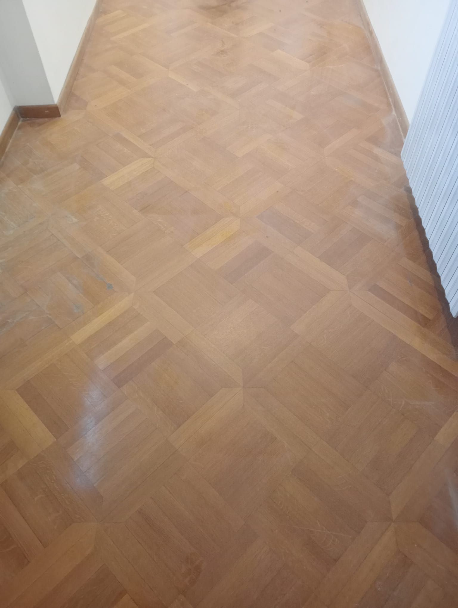 Pavimento in parquet di legno con motivo quadrato, dal caldo colore marrone e dalla finitura lucida.