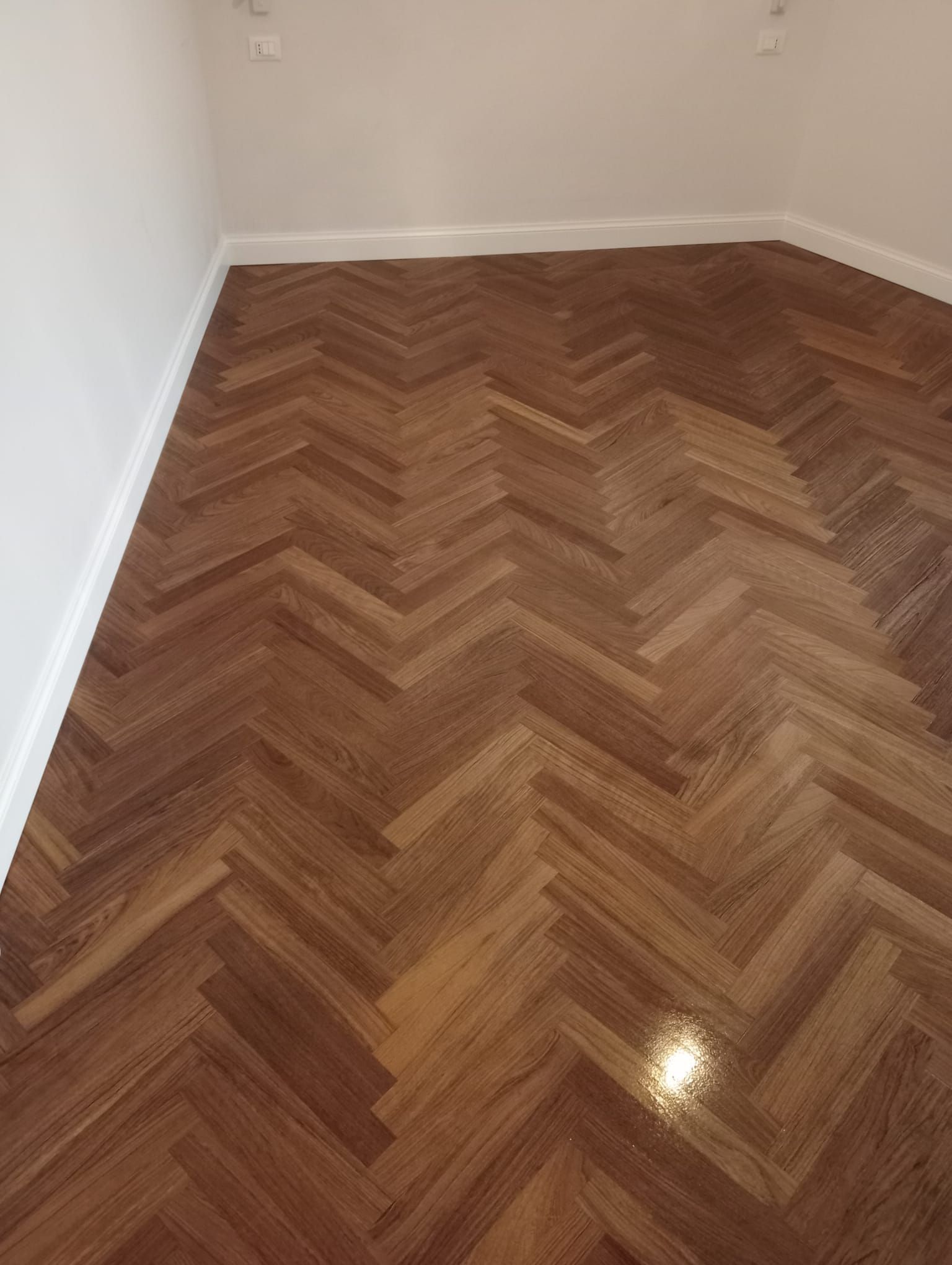 Pavimento in legno a spina di pesce in una stanza con pareti e battiscopa bianchi.