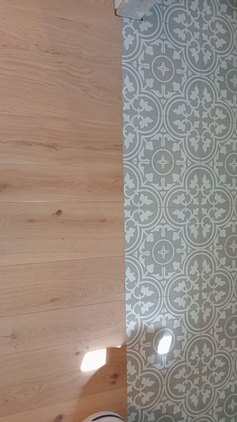 Pavimento in legno chiaro accanto a un pavimento in piastrelle grigie e bianche con motivi geometrici