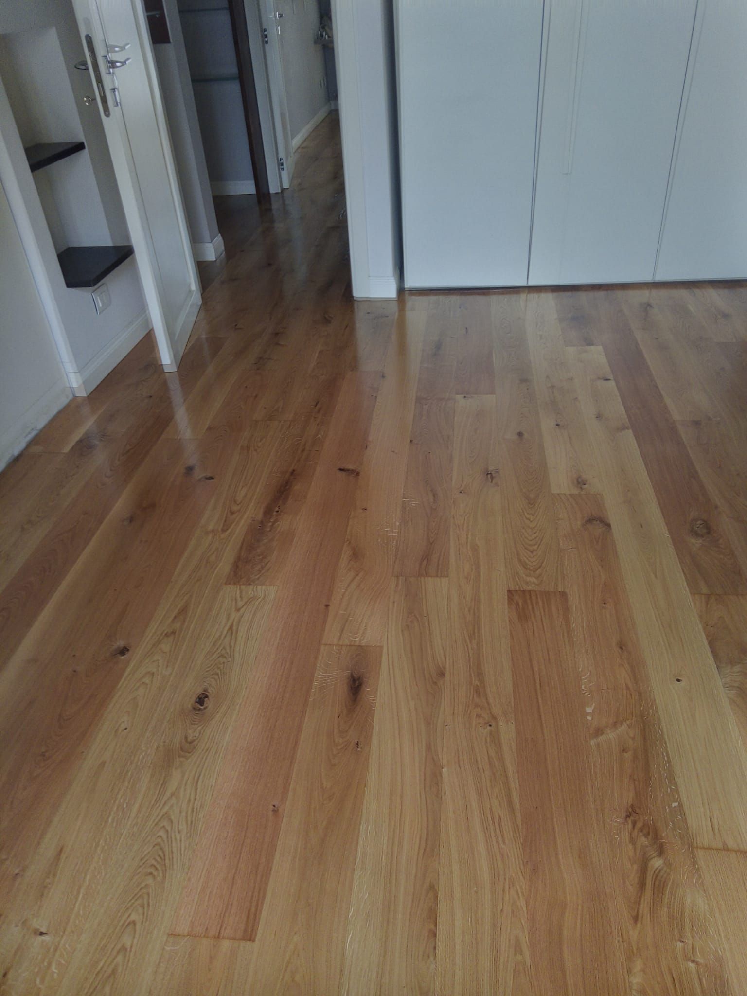 Pavimento in legno in una stanza con pareti bianche e scorcio di corridoio.