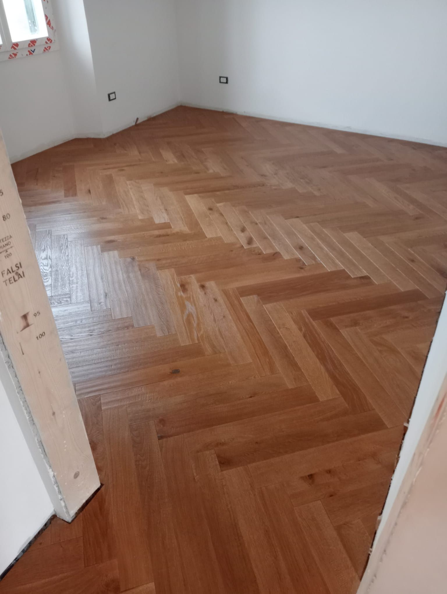 Pavimento in legno a spina di pesce in una stanza vuota con pareti bianche.