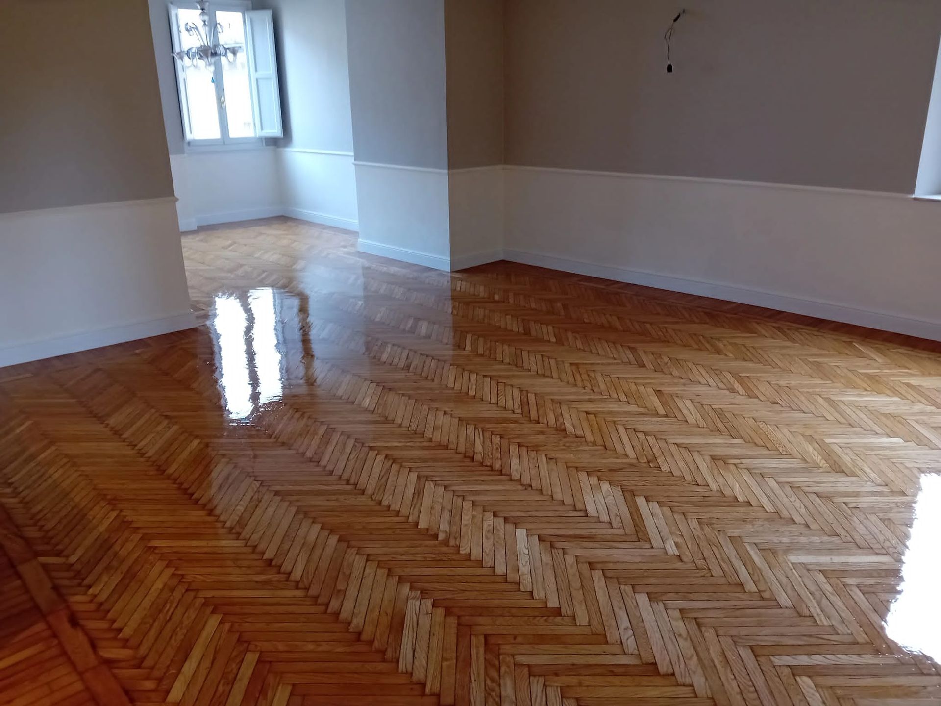 Una stanza con un pavimento in legno a spina di pesce lucido, color marrone chiaro, pareti beige e una finestra.