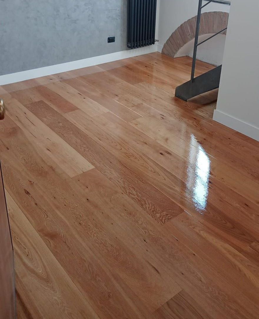 Pavimento in legno massello lucidato con tonalità marrone chiaro che riflettono la luce della stanza.