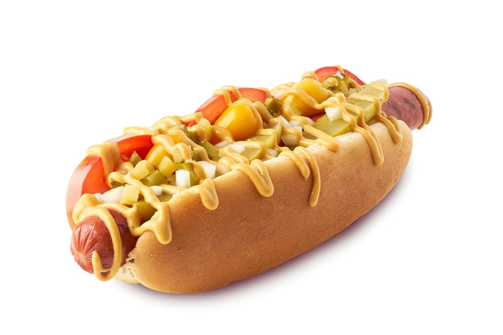 Hot dog on a bun, topped with mustard, diced tomatoes, pickles, and relish.