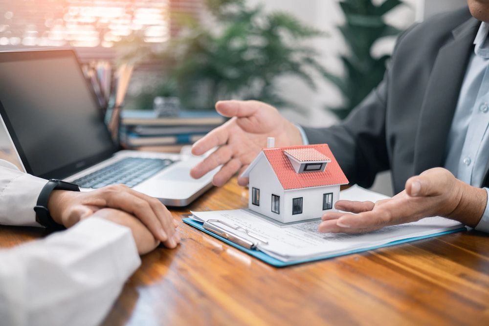 Two People at a Desk, Reviewing Paperwork With a Model House — Into Finance Lending Solutions in Coomba Bay, NSW