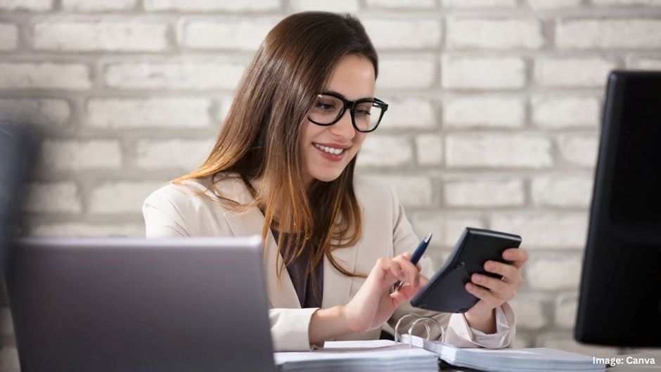 Woman Wearing Glasses, Smiling, Using a Calculator at a Desk — Into Finance Lending Solutions in Coomba Bay, NSW