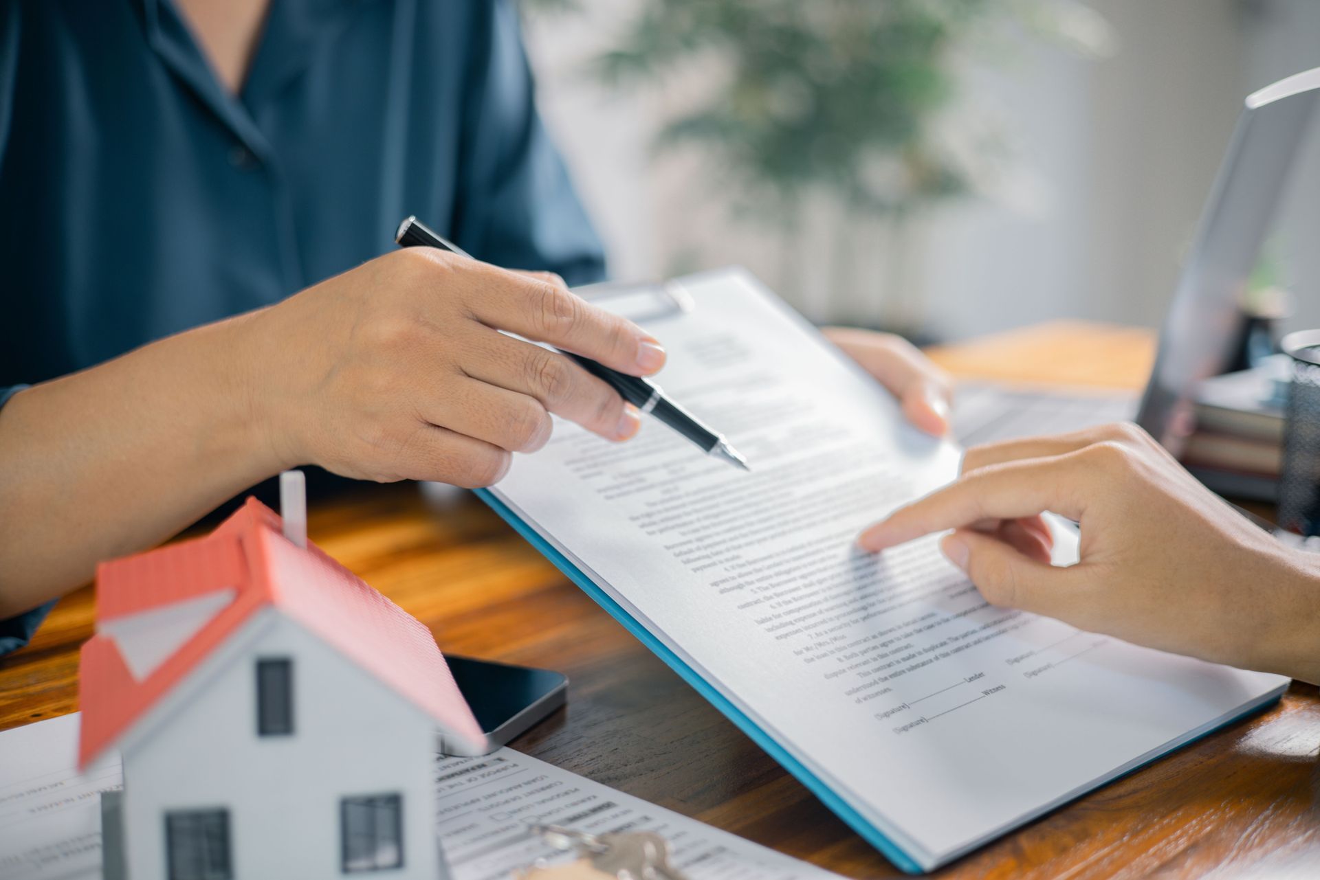 Hands Pointing to a Document With a Pen, Next to a Toy House — Into Finance Lending Solutions in Coomba Bay, NSW