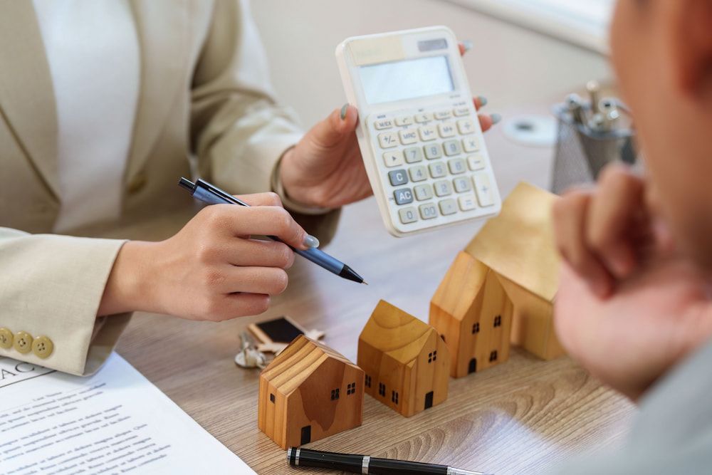 Person Points at Calculator, Showing Results to Another, Miniature Houses — Into Finance Lending Solutions in Coomba Bay, NSW
