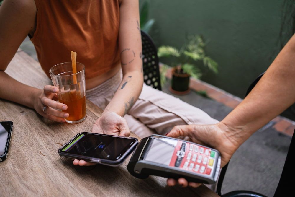 Person Paying With Phone Held Over Payment Terminal at Outdoor Table — Into Finance Lending Solutions in Old Bar, NSW