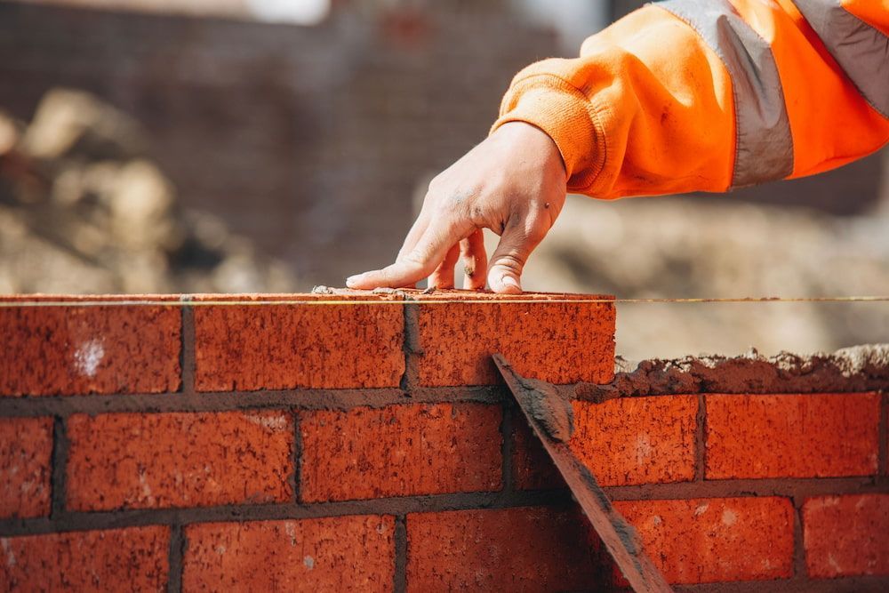 Bricklayer's Hand on a Red Brick Wall, Wearing an Orange Safety Jacket — Into Finance Lending Solutions in Taree, NSW